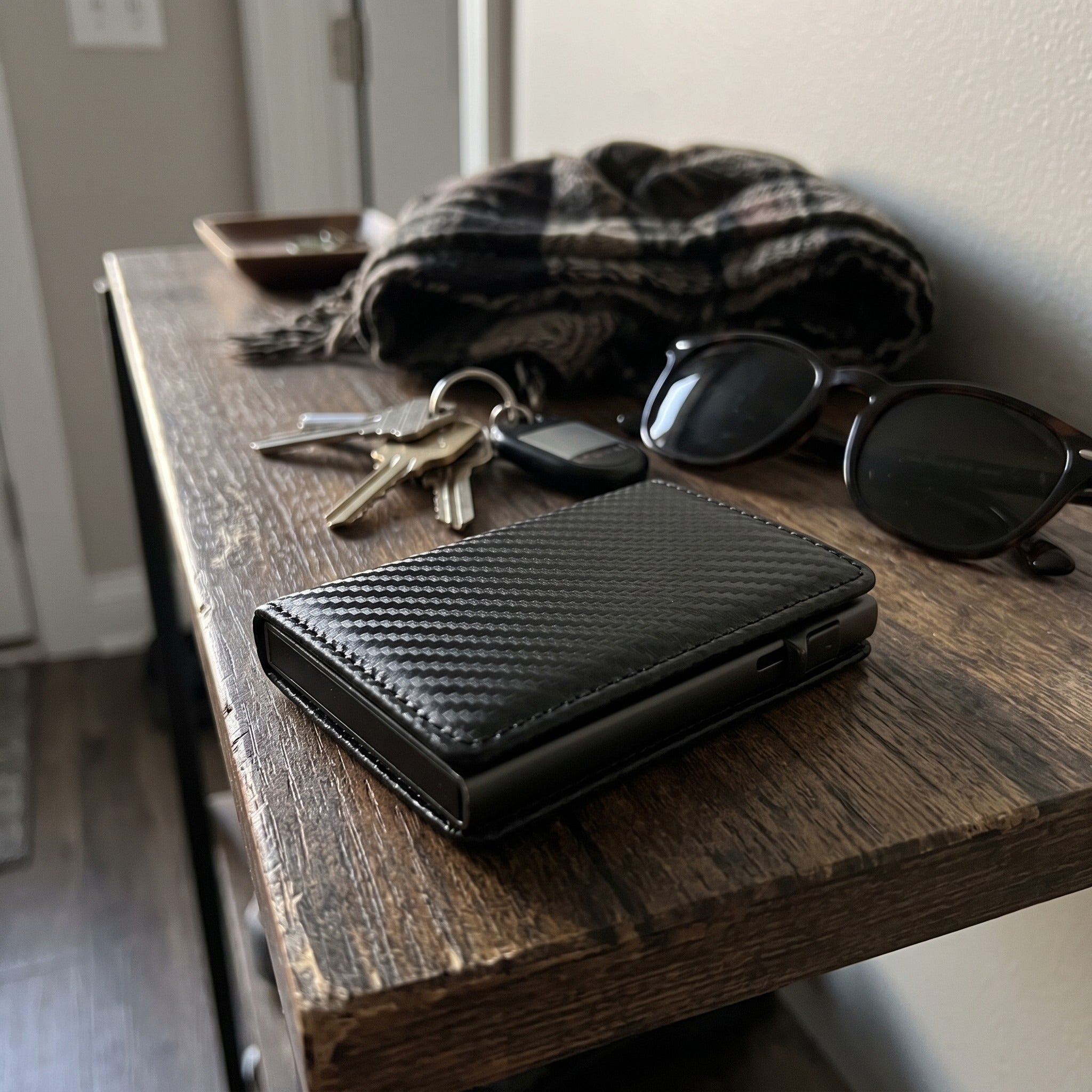 Closed carbon-pattern wallet on an entryway table